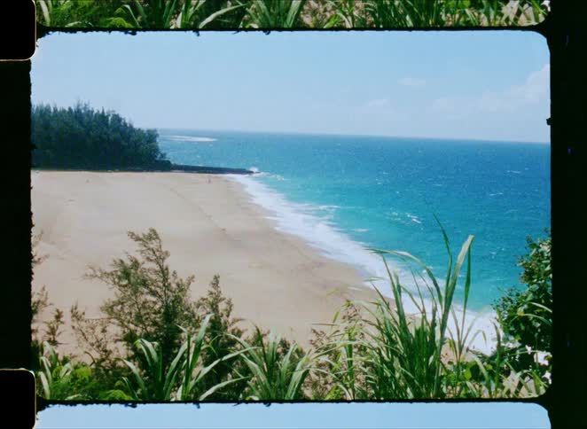 A vintage Super 8 film view from a scenic overlook shows a deserted tropical beach and the blue ocean on a sunny day