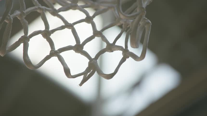 A basketball swishes through the net in a slow-motion, low-angle shot inside a gym