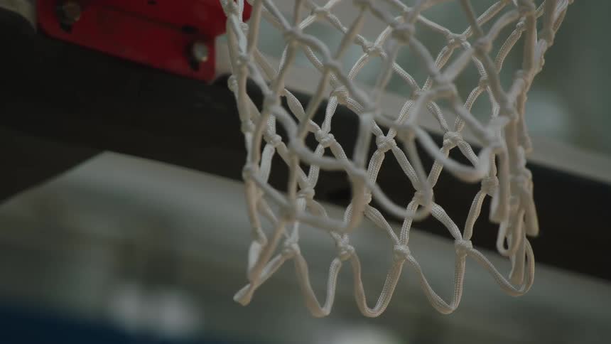 A close-up, slow-motion view shows a basketball swishing perfectly through the net on an indoor court