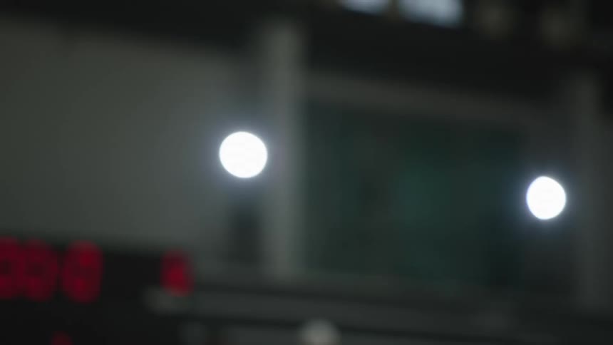 A basketball is dribbled in slow motion on a court with the scoreboard blurred in the background