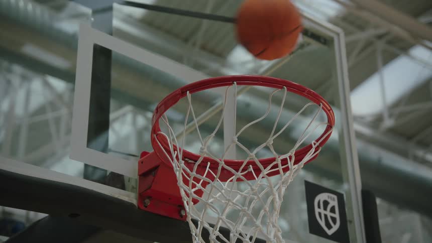 A close-up slow-motion shot of a basketball bouncing off the backboard and rim, missing the shot in an indoor gymnasium