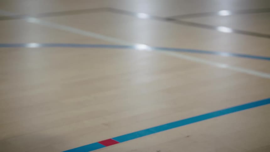 A basketball player with tattooed arms picks up a basketball and dribbles it on an indoor court, with the camera focusing on the bouncing ball