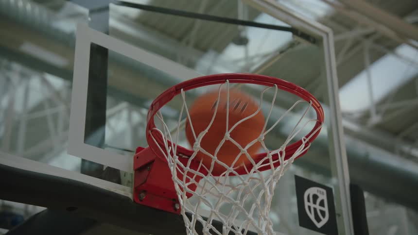 A slow-motion close-up captures a basketball swishing through the hoop and net in a gym