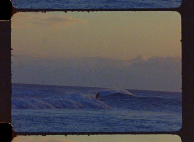 Slow motion shot on vintage film of a solitary surfer carving a wave during a golden sunrise