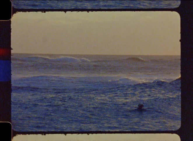A lone surfer rides a breaking wave in the ocean at sunrise, captured on vintage super 8mm film