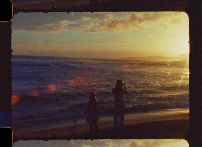 Vintage film captures the silhouette of a mother and daughter watching the golden sunset over the ocean waves