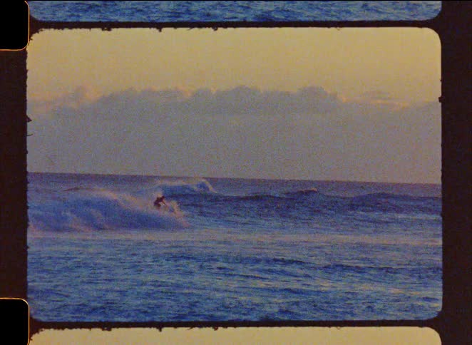 Vintage Super 8 film captures surfers riding powerful ocean waves during a golden sunrise
