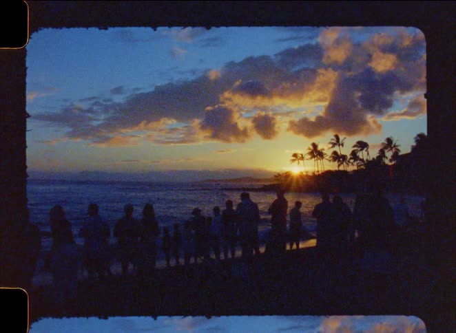 Vintage footage captures a group of silhouetted people watching a beautiful tropical sunset over the ocean