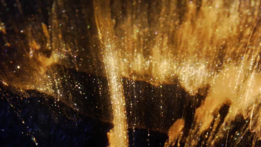 A macro shot shows sparkling gold and multicolored glitter flowing through a viscous liquid against a dark background