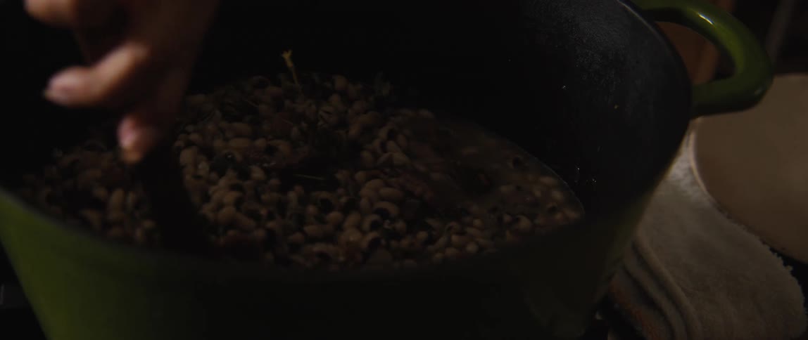 A close-up slow-motion shot of a hand using a wooden spoon to stir a pot of simmering black-eyed peas