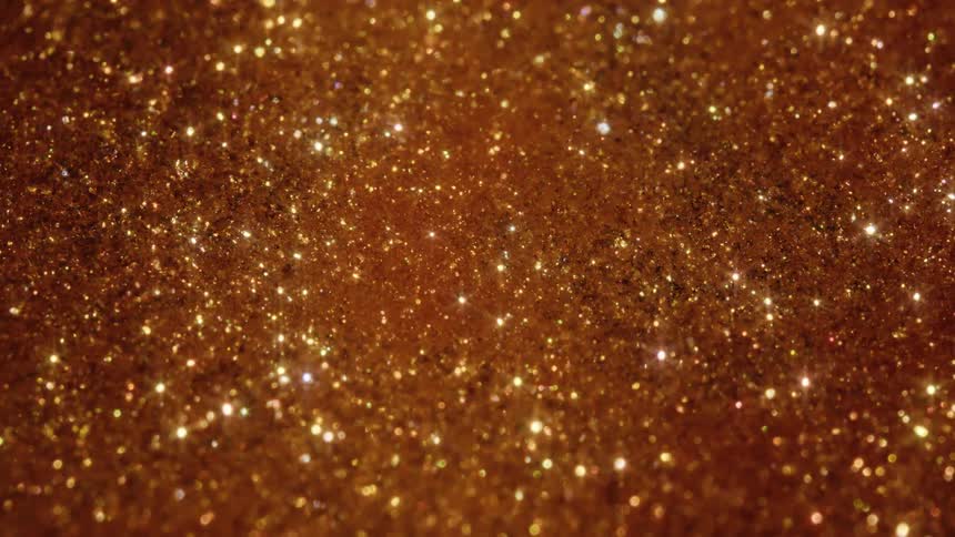 Shimmering gold glitter particles twinkle in a mesmerizing close-up abstract background