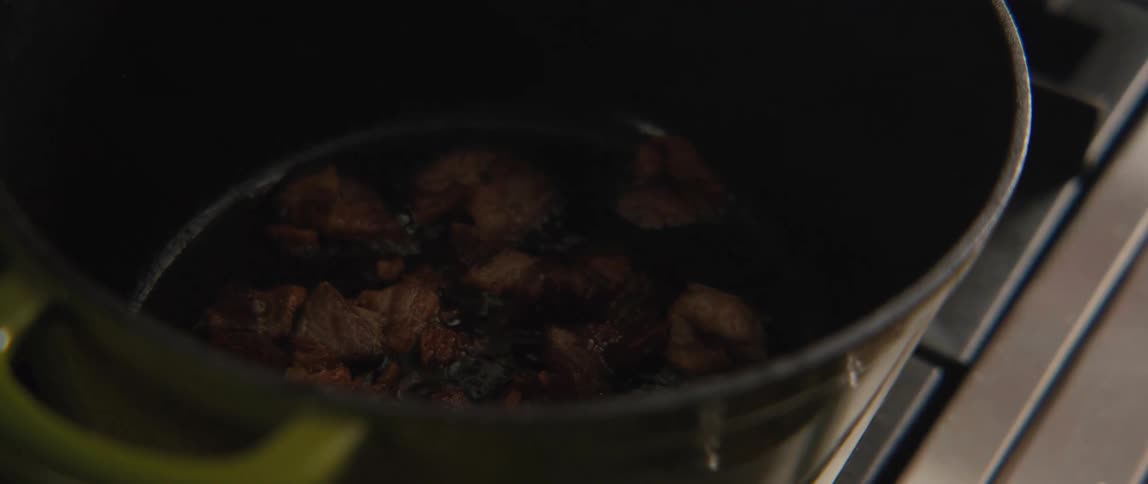 Cubed pork sizzles and fries in hot oil inside a dark pot on a stovetop