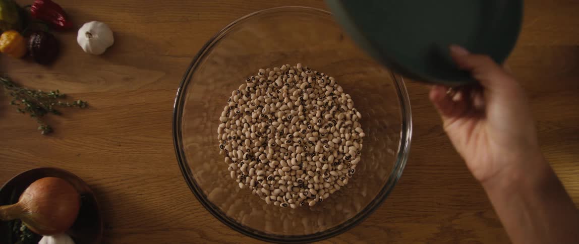 Slow-motion overhead shot of black-eyed peas being poured into a large glass bowl