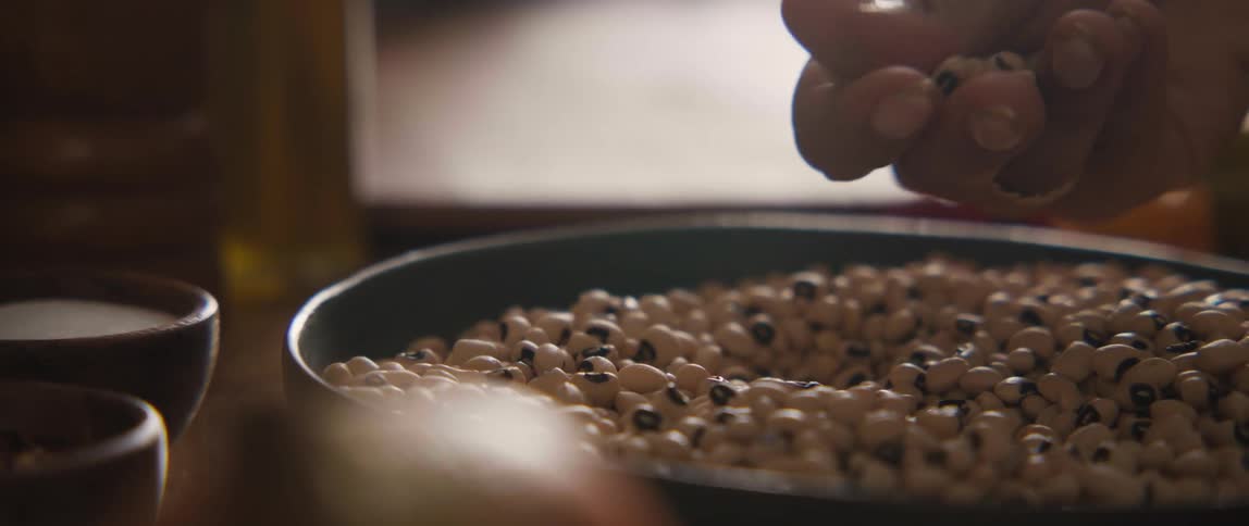 Slow motion close-up of a hand scooping and sorting dry black-eyed peas in a bowl