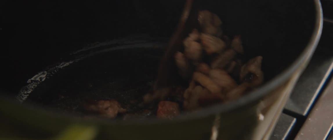 Sizzling pieces of meat are stirred with a wooden spoon and browned in a hot pot