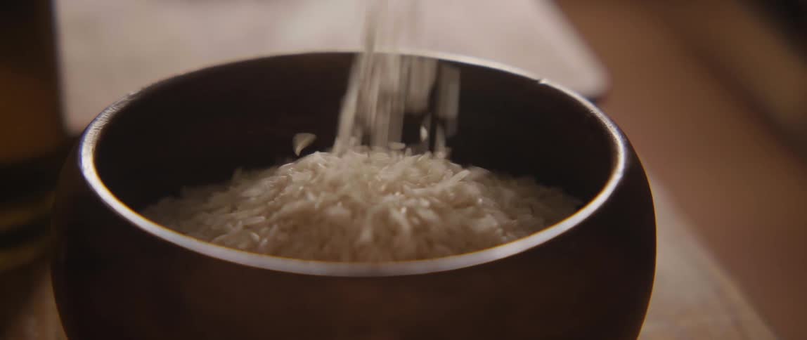 Slow motion close-up of white rice being poured into a dark wooden bowl