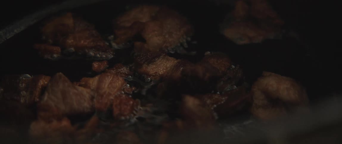 An extreme close-up slow-motion shot shows pieces of pork belly frying and sizzling in hot, bubbling oil