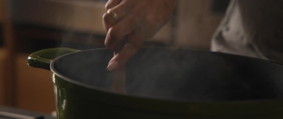 Slow motion close-up of a chef stirring a large pot of steaming food with a wooden spoon