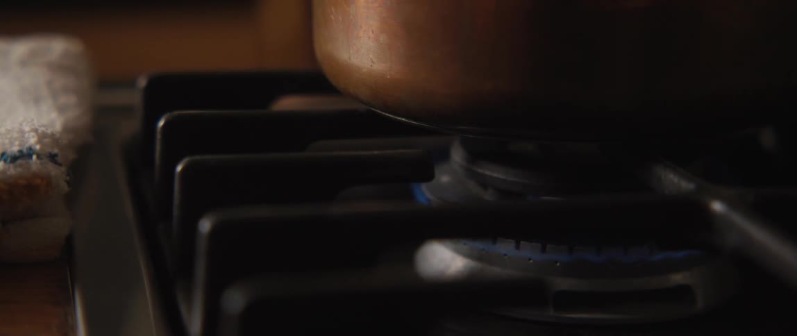 A close-up of a blue gas flame flickering under a copper pot on a kitchen stovetop