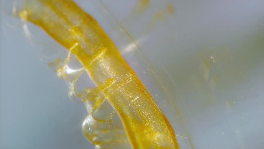 A shimmering gold liquid with sparkling particles slowly flows in an abstract, mesmerizing pattern