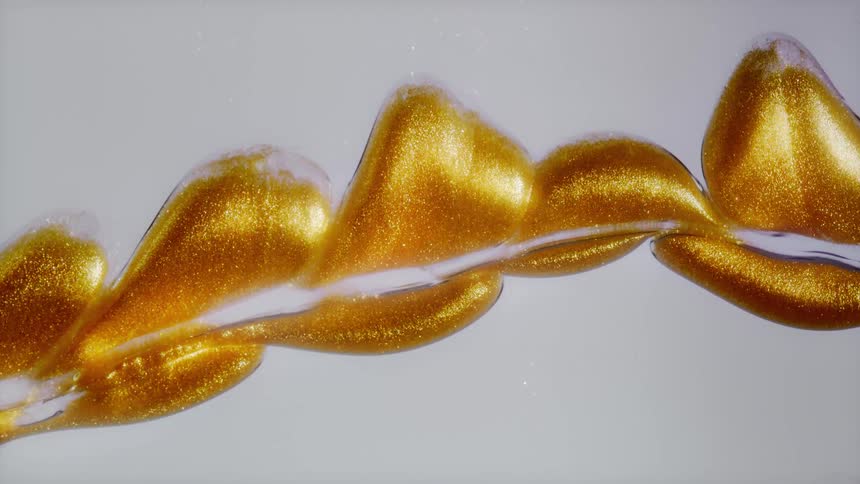 Luxurious golden glitter paint slowly flows and swirls on a white background in a mesmerizing abstract display