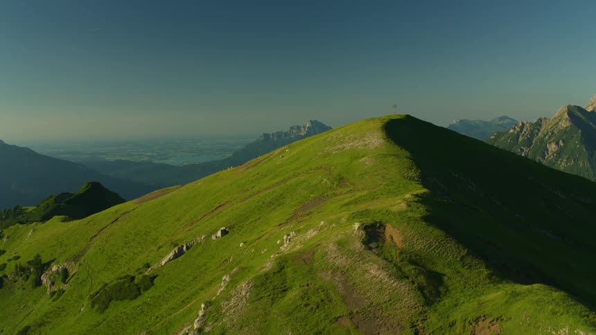 A green mountain peak with mountain range in distance