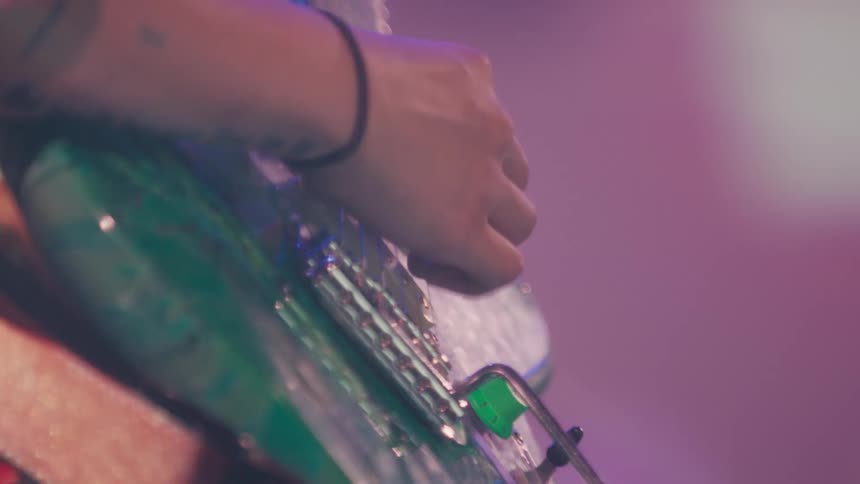 A dreamy close-up shot of a musician's tattooed hand strumming an electric guitar during a live performance