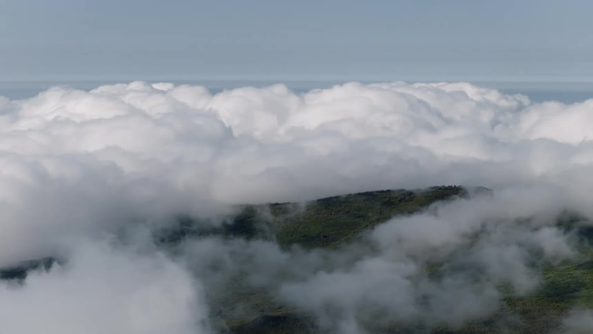 A majestic, static view from high above shows a green mountain peak poking through a dense sea of white clouds