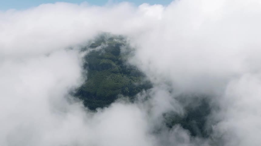 A breathtaking view through an opening in the clouds reveals a lush green forested mountain peak below
