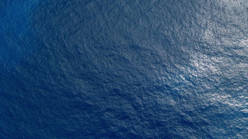 Calm, deep blue ocean water gently ripples under a soft sun glare in this top-down aerial animation