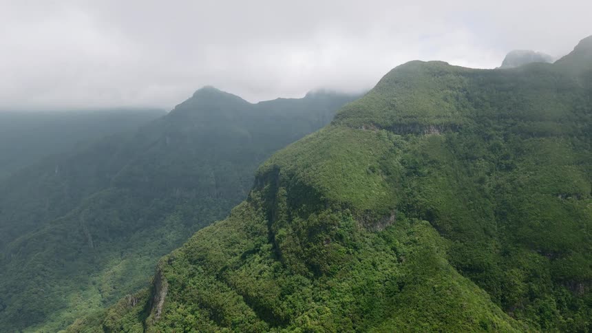 A wide aerial view of majestic green mountains covered in lush forest and shrouded in thick fog