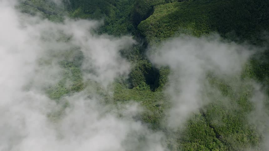 A breathtaking high aerial view peers through a veil of clouds to reveal a lush, green mountain valley below