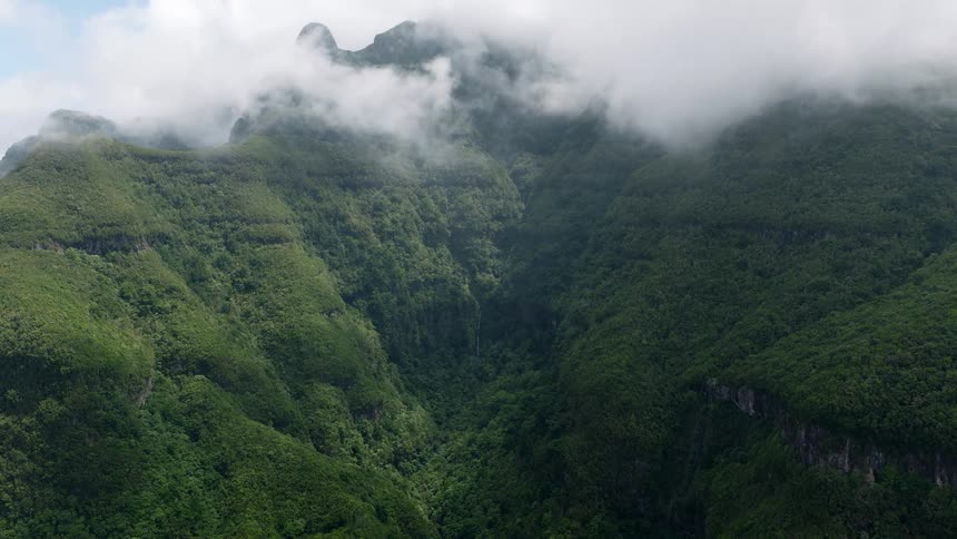 Misty clouds drift over the peaks of a vast, green mountain range covered in a dense forest