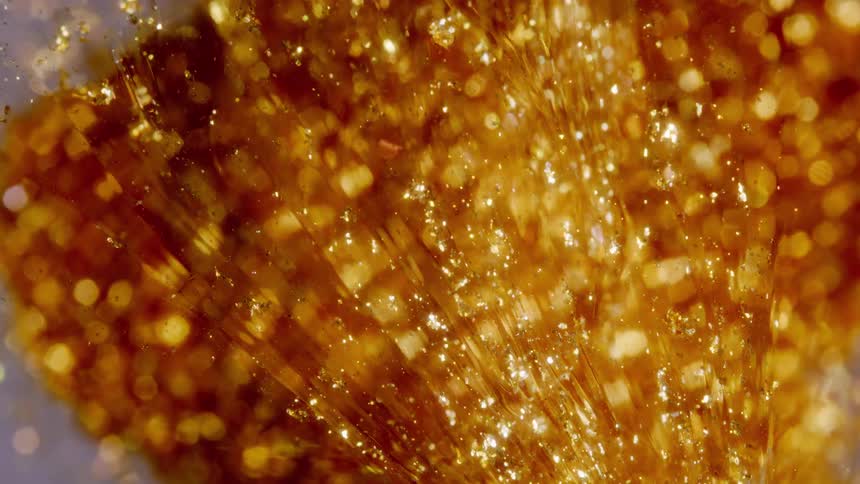Close-up of sparkling gold dust and fine strands moving through a glowing, viscous liquid
