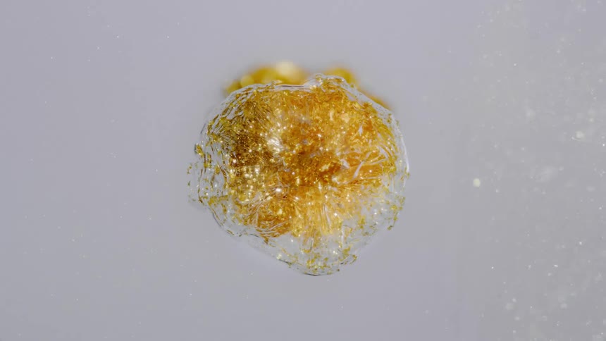 Mesmerizing macro shot of a golden glitter bubble slowly reacting and shimmering on a pristine white surface