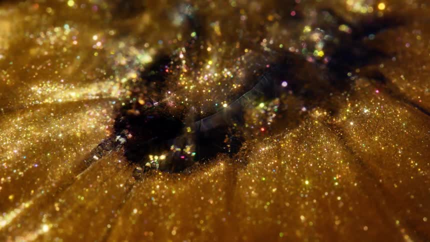 A mesmerizing macro shot of shimmering golden and iridescent glitter flowing slowly with dark ink