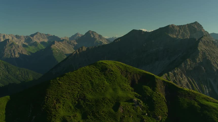 A cross is on top of these green mountains