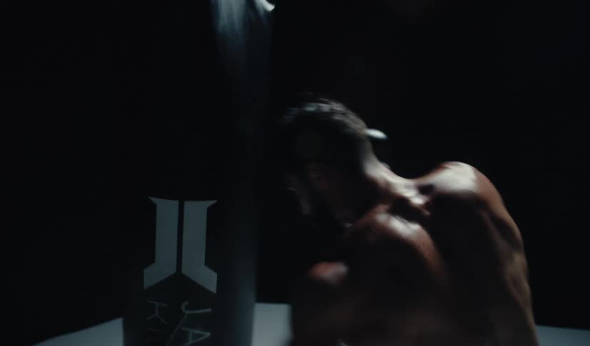 A muscular boxer in gloves relentlessly punches a heavy bag in a dark, dramatically lit room