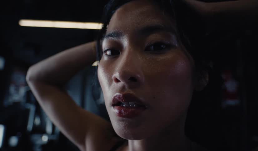 Intense close-up portrait of a sweaty athletic woman looking at the camera in a dark gym