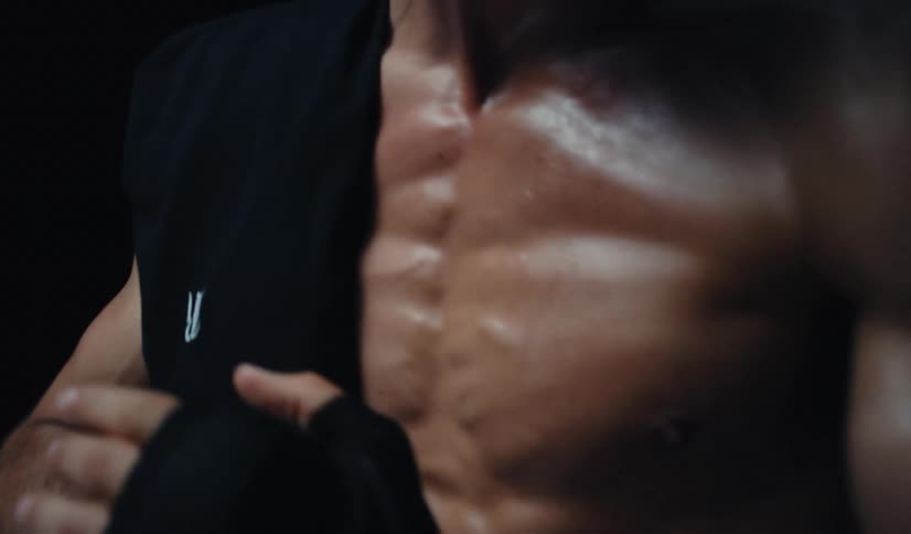 Close-up of a sweaty, muscular fighter's torso and hand wraps in a dark, moody setting