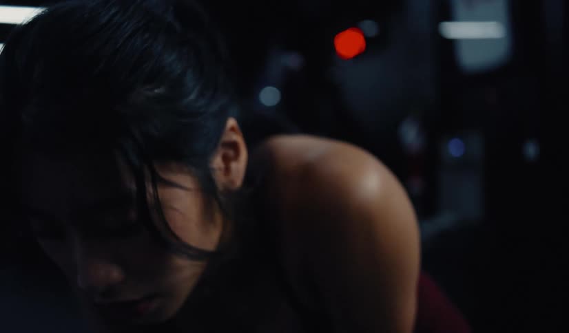 A determined athletic woman breathes heavily while taking a break from her intense workout in a dark, atmospheric gym