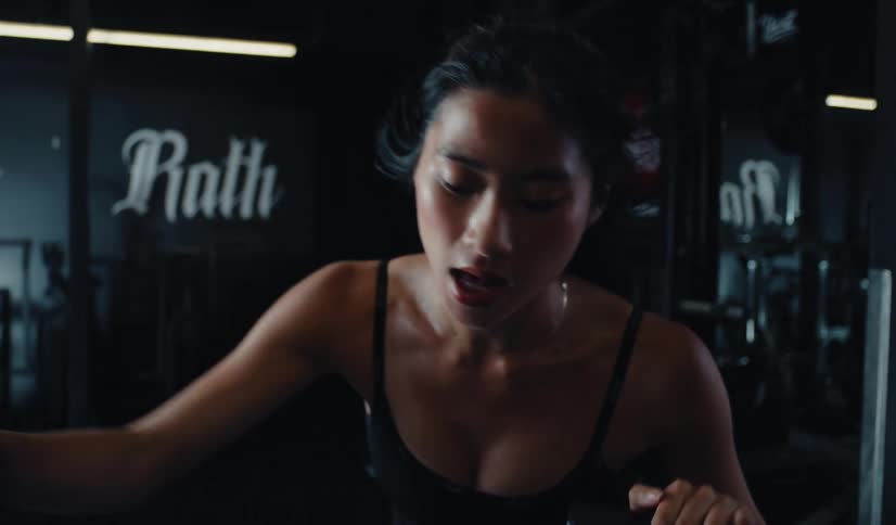 Slow-motion close-up of a determined woman sweating and breathing heavily during an intense cardio workout in a dark gym