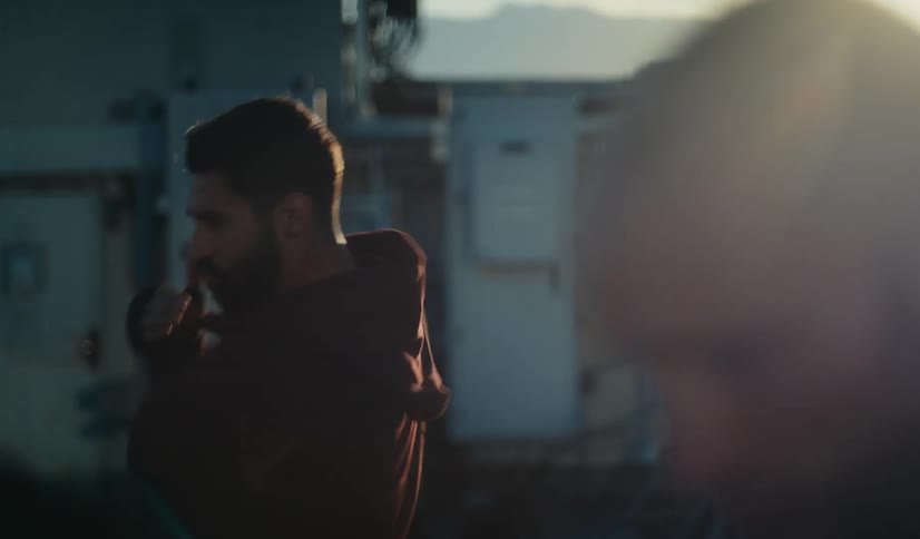 A focused boxer in a red hoodie shadowboxes on a rooftop at sunset in dramatic slow motion