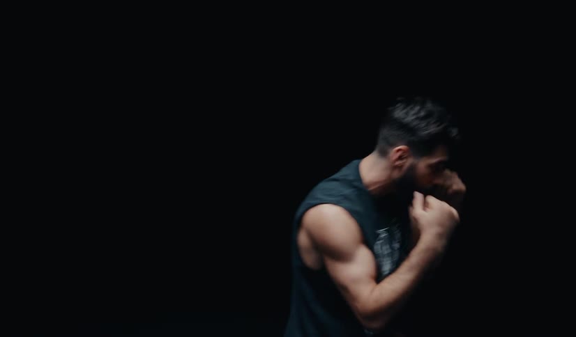 A muscular man shadowboxes in slow motion, throwing punches in front of a black background
