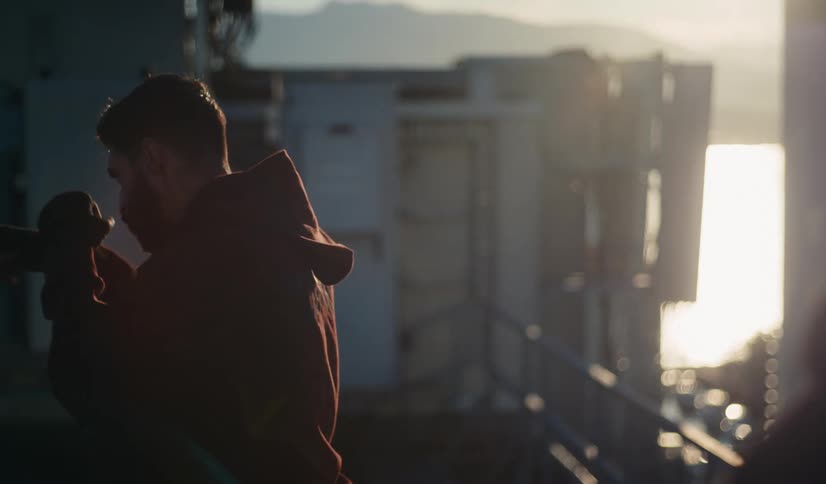 A determined male boxer in a red hoodie shadowboxes in slow motion on a rooftop during a beautiful sunset