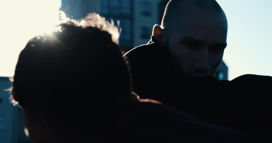 An intense bald boxing coach holds pads for his training partner in a dramatic slow-motion shot with a bright lens flare
