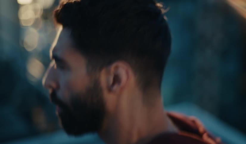 A determined bearded man in a red hoodie performs intense push-ups during a workout, captured in a cinematic close-up
