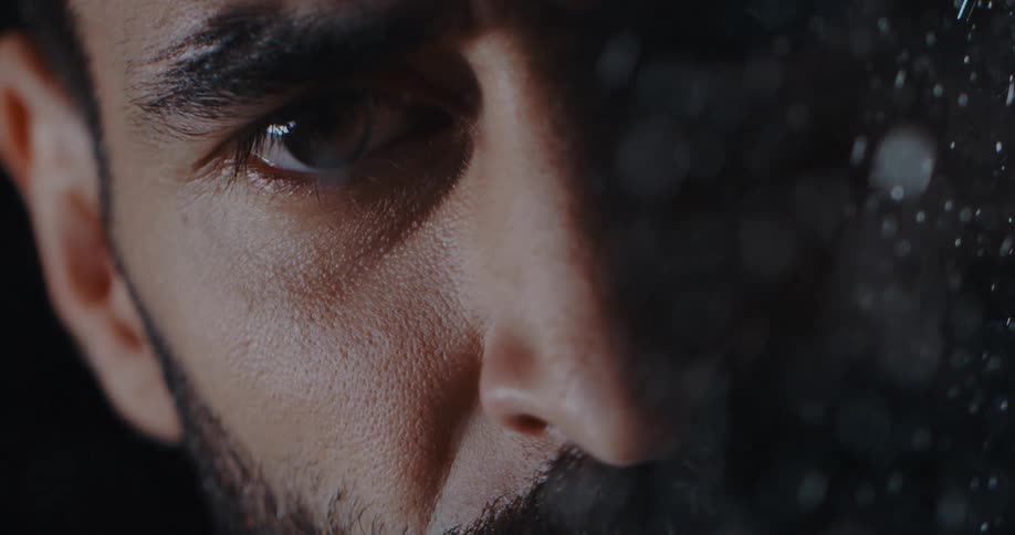 Cinematic slow-motion close-up of a bearded man's intense gaze during a snowfall at night