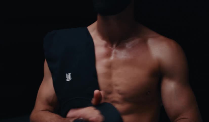 Intense slow motion portrait of a muscular, bearded man with a t-shirt over his shoulder, recovering after a workout against a dark background