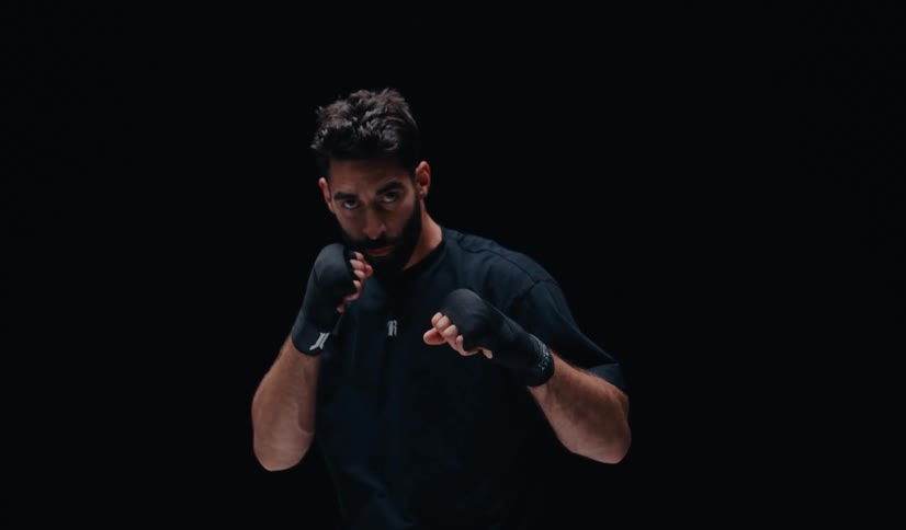 A slow-motion shot of a male boxer with a beard getting into a fighting stance against a black background